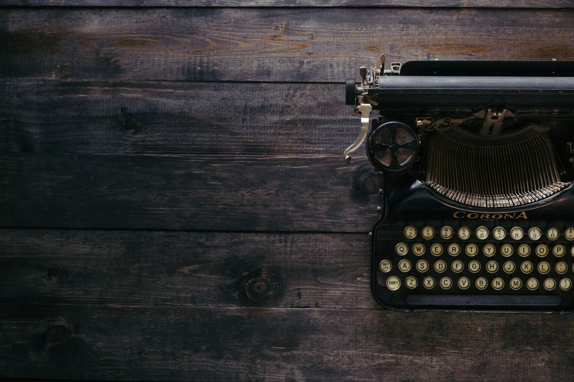 An old-school typewriter sitting on a dark-stained wood surface.