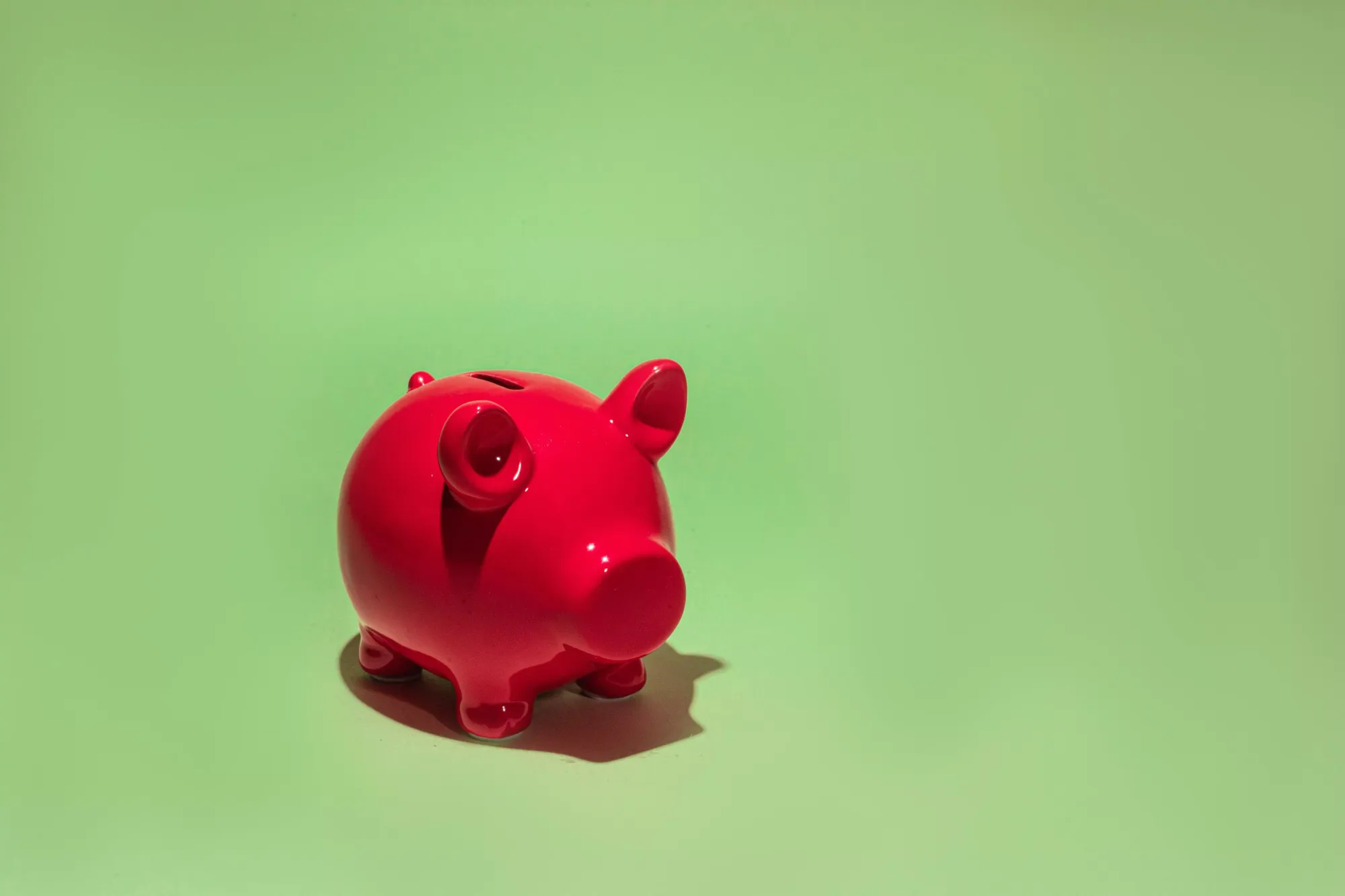 A small, red, ceramic piggy bank against a bright green backdrop.
