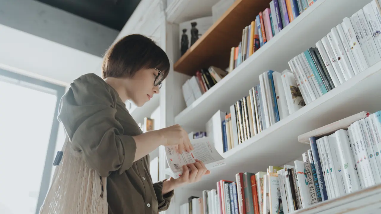 Woman in gray coat reading books in bookshop.