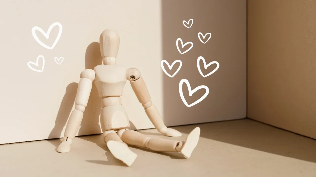  Wooden puppet character sitting against neutral background with floating white hearts.