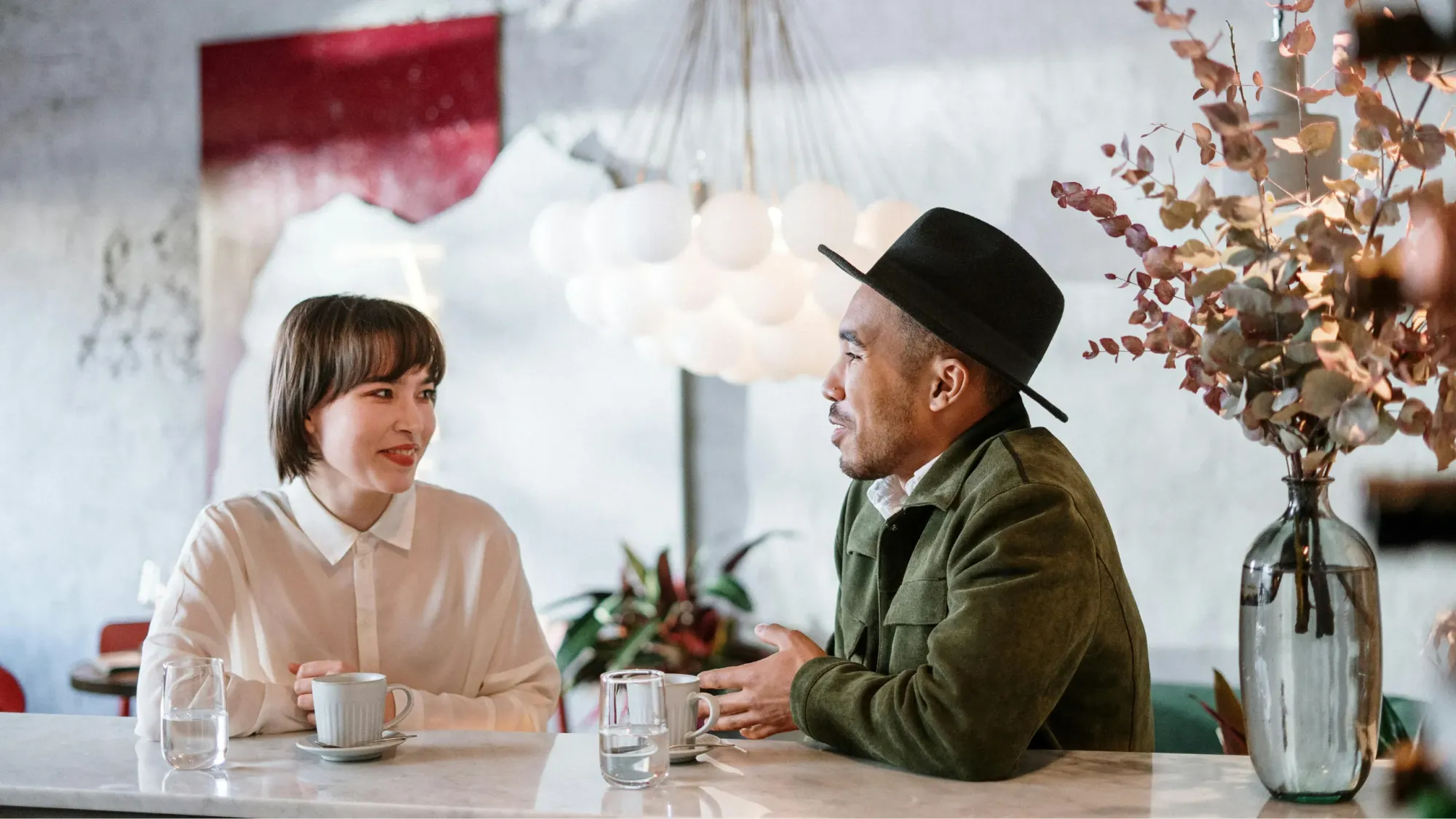 Man in green jacket sitting beside woman in white dress shirt in light-styled cafe.