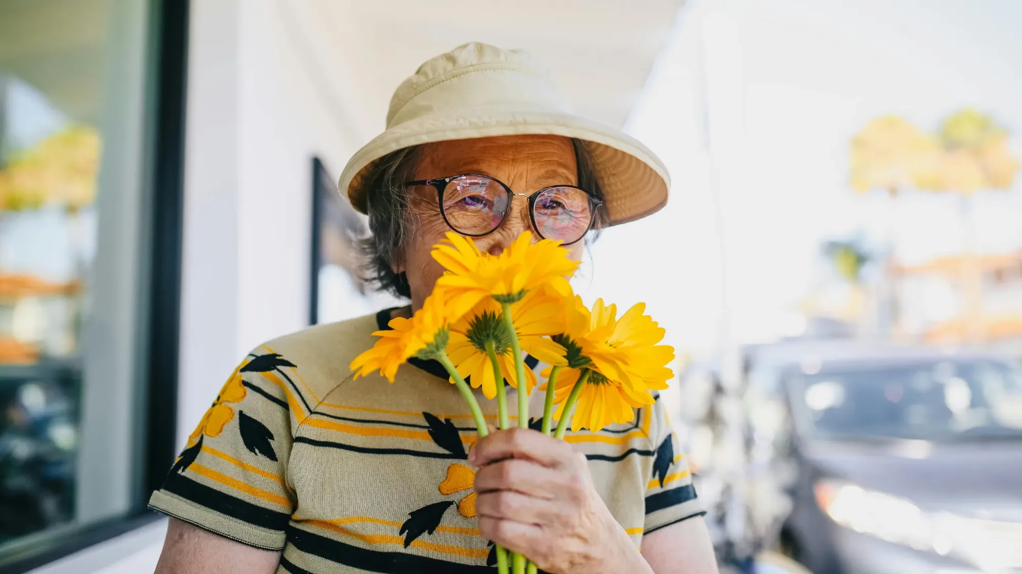 Eldery woman smelling yellow daisy flowers.