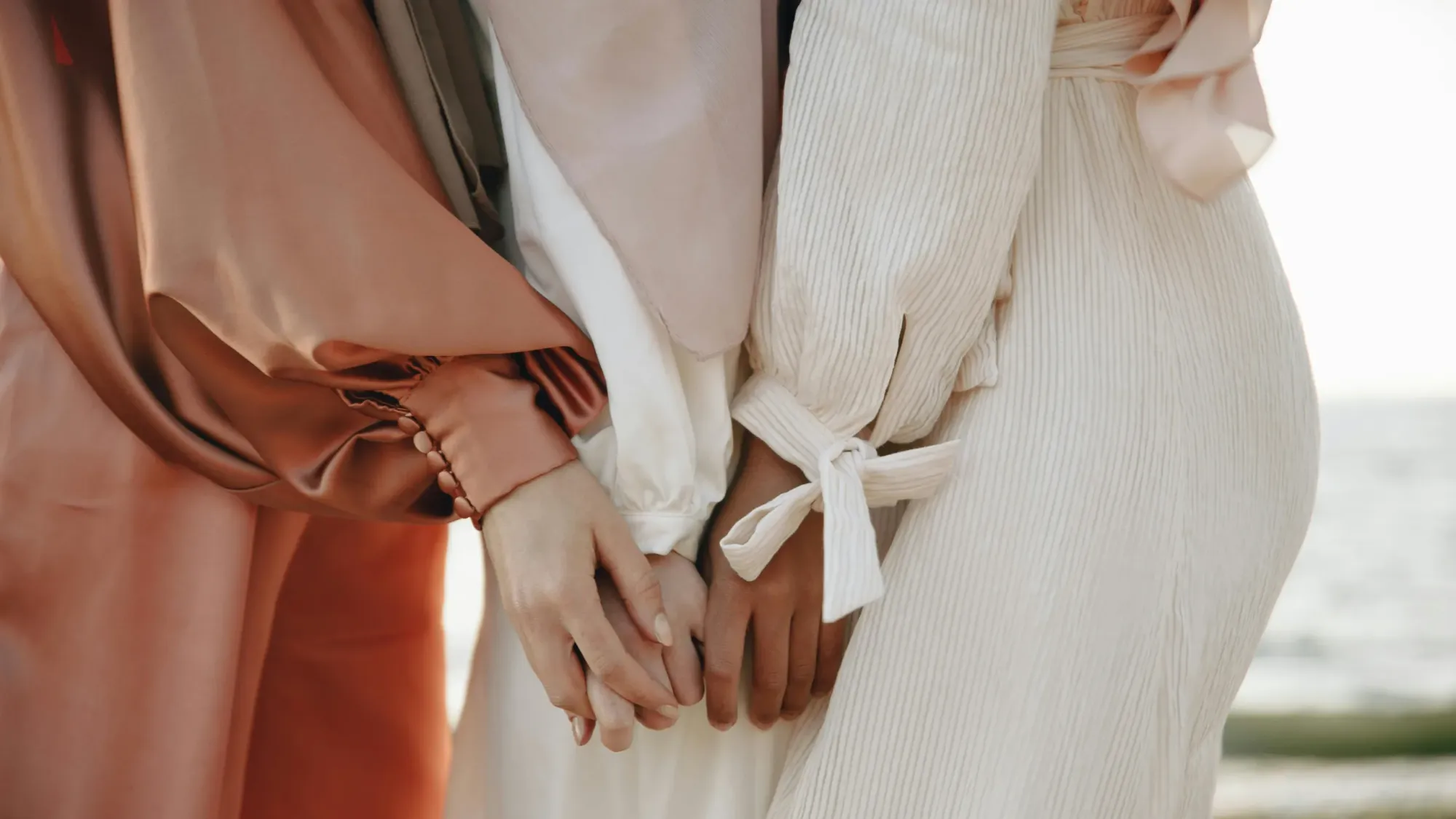 Women wearing dresses of different textures and holding hands.